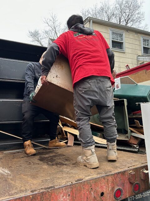 Professional junk removal team lifting old furniture into a truck during residential cleanout in long island.